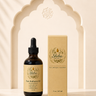 A bottle of Shiba Organics Pure Radiance Oil next to its matching beige cardboard box, set against a decorative beige arch background with soft leaf shadows.