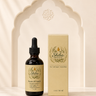 A bottle of Shiba Organics Roots of Youth dark aging arumetin oil next to its beige packaging box, displayed on a beige stone surface in front of a decorative archway.