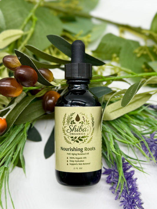 Bottle of Shiba Organics Nourishing Roots oil with a dropper surrounded by green leaves and purple flowers.