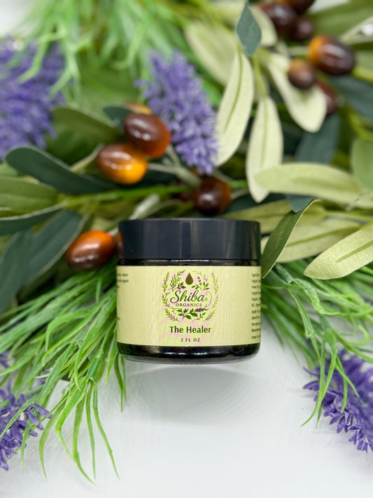 Jar of 'The Healer' with Shiba branding surrounded by green leaves and purple flowers on a white background